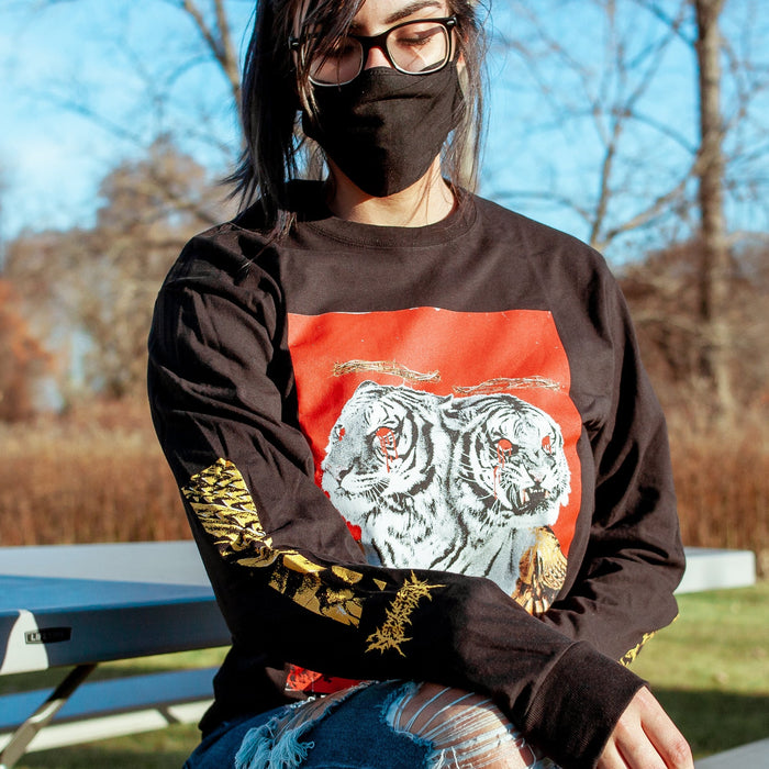 Someone wearing the Long sleeve shirt that has an image with a red background and a two headed white tiger with gold wings on the front of the vinyl cover. There are also red roses at the bottom of the cover, blood coming from both tiger’s eyes, and a crown of thorns above both of the tigers heads. On the sleves which contain gold lettering for the band POLYPHIA