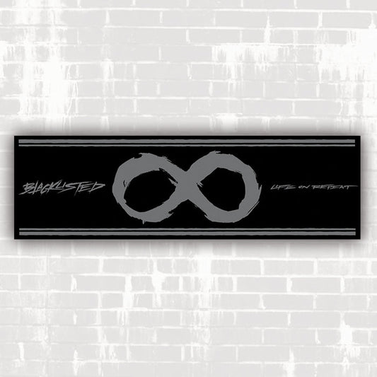 A rectangular black banner displays a large grey infinity symbol at its center, with "LIFE ON REPEAT" in stylized text on the right, all set against a white brick wall background. Brand: Life On Repeat.