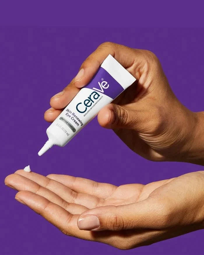 CeraVe Skin Renewing Eye Cream 15ml tube dispensing cream into a hand against a purple background.