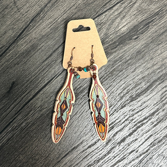 Feather-shaped earrings with colorful designs on a wooden surface.