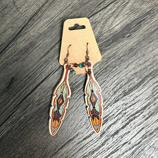 Feather-shaped earrings with colorful designs on a wooden surface.