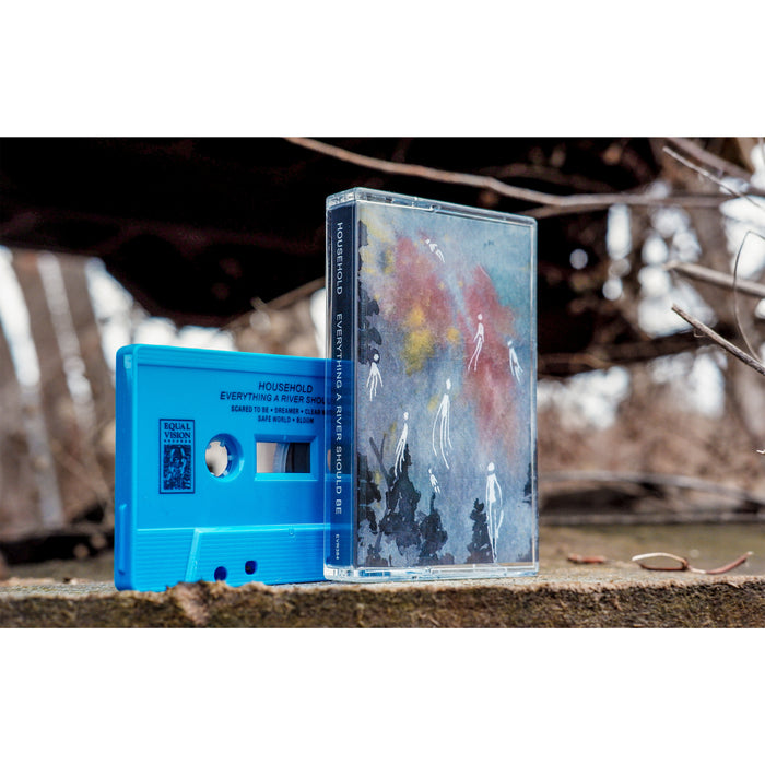 A blue Household cassette tape and its case with abstract artwork stand on a rough outdoor surface, while blurred branches and rusty metal fade in the background.