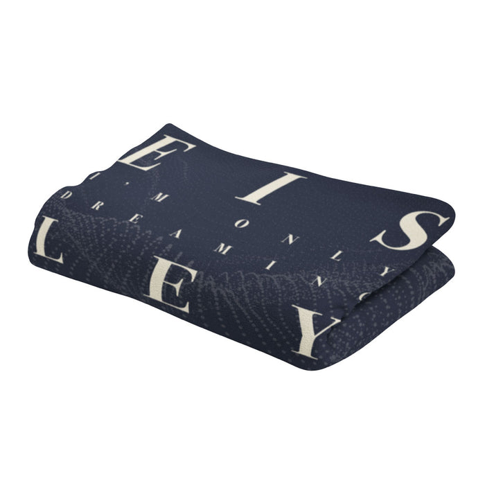 A dark blue Eisley Dreaming blanket with large white letters and partial words, including "ONLY DREAMING." The soft, cozy fabric makes it perfect for relaxing moments.