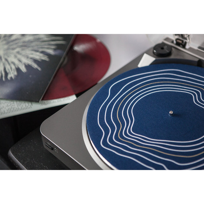 A close-up of a Gatherers record player with a blue Lines Slip Mat featuring white concentric lines. A maroon vinyl record and its cover are partially visible nearby.