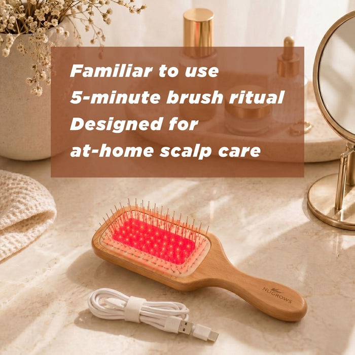 NuGROWS VivaBrush Pro laser scalp brush with red light activated, USB cable, on beige marble surface with mirror and flowers.