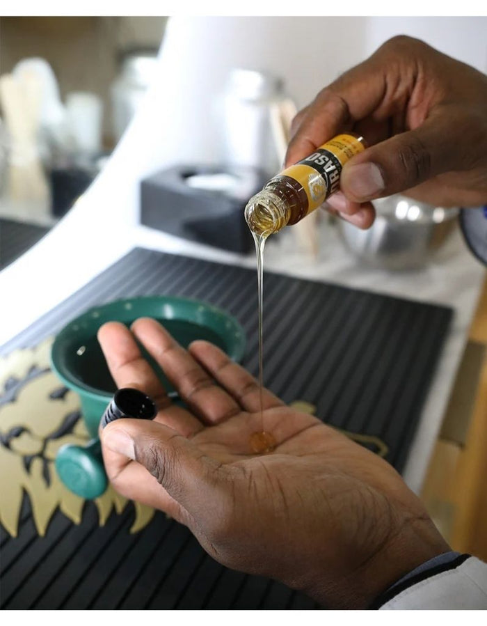 Person pouring Proraso beard oil from a small bottle into their palm, showing the oil's golden color, on a kitchen countertop