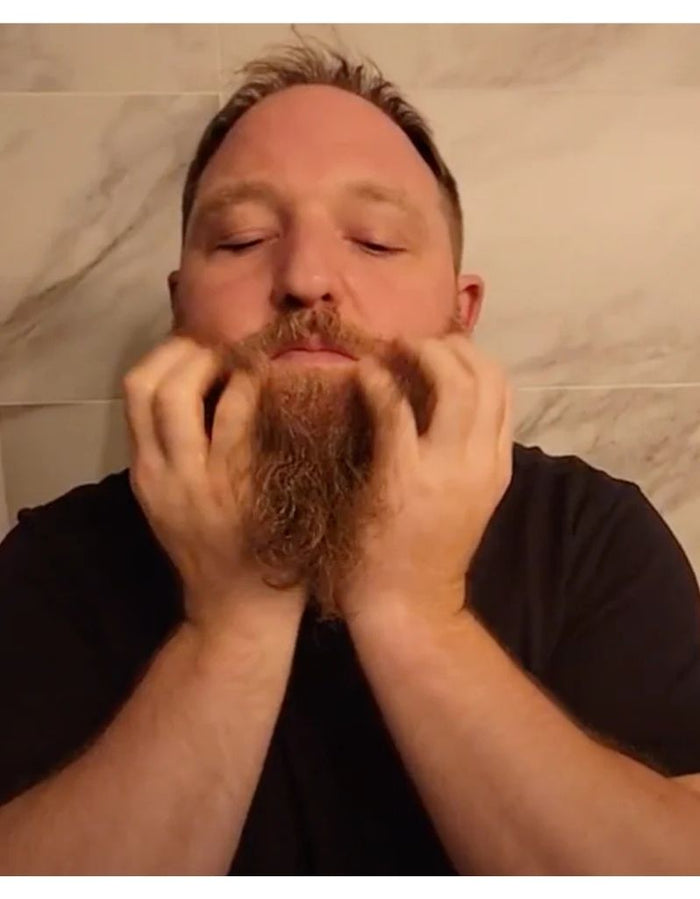 Man with a full beard and mustache, gently massaging his beard, demonstrating the use of Proraso Hot Oil Beard Treatment for grooming